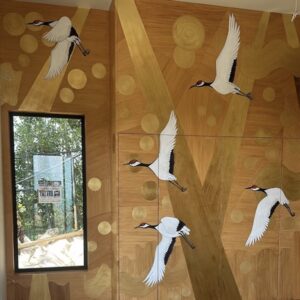Interior mural in London with flying white cranes, and golden accents on a wood-textured background
